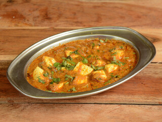 Paneer Butter Masala or Cheese Cottage Curry, served over a rustic wooden background, selective focus