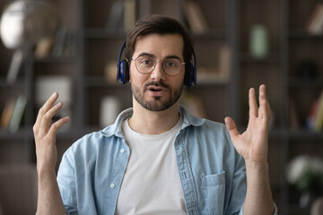 Close up screen portrait view of young Caucasian man in headphones talk on video call with client....