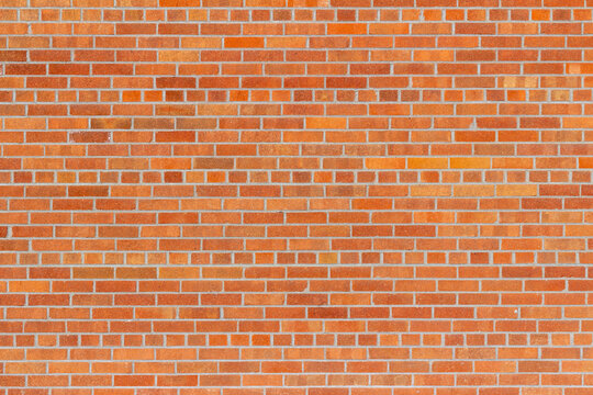 Full frame texture background of a grungy vintage brick wall in common bond pattern, with bricks in varying shades of orange and red, having a subtle shimmering surface patina.