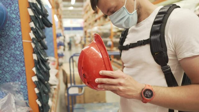 Close-up of hand caucasian male worker holding red orange helmet hard hat in hardware store background. Engineering concept and architectural equipment, theme of safety construction engineering work