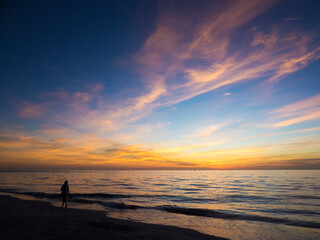 Young woman walking on a Gulf of Mexico beach at St. Pete Beach, Florida at sunset with a dramatic orange sunlit sky.