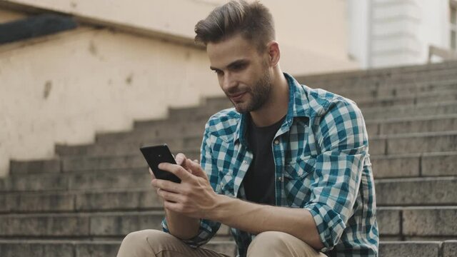 Young optimistic man using mobile phone outdoors on the street