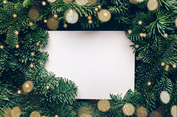 Fototapeta na wymiar Holiday background with white card in the middle of evergreen tree branches, christmas and festive season concept, minimalistic design, copy space