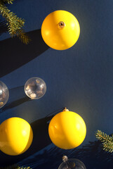 Decoration yellow and transparent balls decoration, spruce branches on dark blue background with long shadows. New Year's or Christmas concept. Winter holiday theme. Space for text. Flat lay, top view