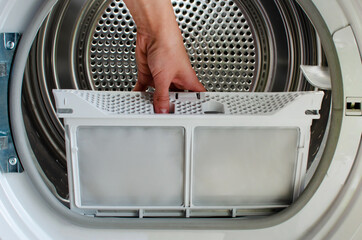 A housewife holds a lint trap from a front-loading tumble dryer. Woman's hand