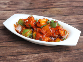 Paneer Manchurian is Indo Chinese cuisine dish, Paneer cubes tossed with tomatoes, onions, spring onions, sesame seeds and soy sauce. served over a rustic wooden background, selective focus