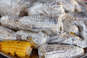 close up shot of grilled barbecued sweetcorn cobs covered in foil. Home cooking. baked sweet corn. summer picnic, concept of resting in fresh air. BBQ in garden.