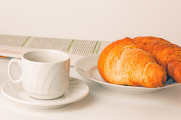 breakfast: a cup of coffee, two croissants on a plate and a morning newspaper on the table