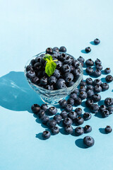 Many Blueberries in crystal vase on blue background. Closeup organic raw vegan dessert food. Banner template