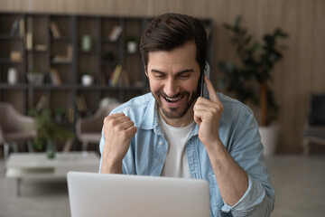 Excited millennial Caucasian man work distant on computer talk on cellphone celebrate online win....