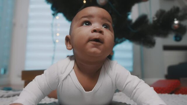 Adorable black baby having a tummy time under the christmas tree surrounded by presents. First baby christmas. High quality 4k footage
