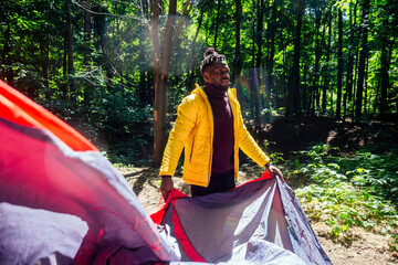 african american in yellow jacker putting on a tent in forest