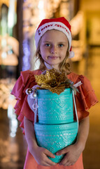 Adorable little girl wearing Santa hat and holding present gift box. Merry Christmas and happy holidays