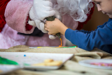 Little boy decorating Christmas biscuits and gingerbread cookies in kitchen together with Santa Claus. Kids cooking class. Merry Christmas and happy holidays