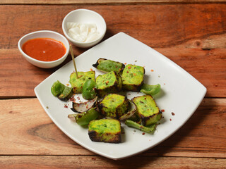 Paneer Tikka Kabab is an Indian dish made from chunks of cottage cheese marinated in spices and grilled in a tandoor. served over a rustic wooden background, selective focus