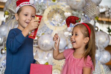 Two adorable little children: brother and sister are exchanging gifts and presents near Christmas tree. Merry Christmas and happy holidays