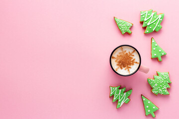 A mug of latte and Christmas gingerbread trees on pink background
