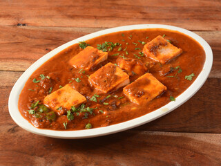 Paneer Tikka Masala is a famous indian dish, served over a rustic wooden background, selective focus