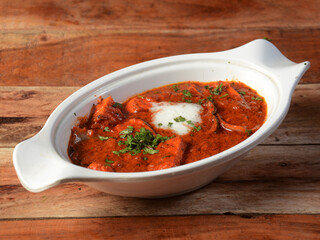 Paneer Tikka Masala is a famous indian dish, served over a rustic wooden background, selective focus