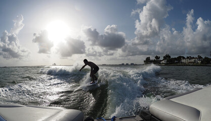 Man's silhouette wake surfing behind boat with sun on the background