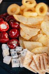 Mix of different snacks and appetizers. Street food plate with set of various kind snacks: bread spicy crackers, french fries and dip, tomatoes, delicious cheese on dark background. antipasto plate