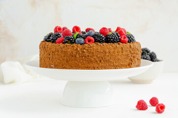 Chocolate honey cake with cream and fresh berries on top on a white plate on a concrete background. Copy space.