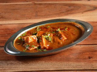 Paneer Masala or Cheese Cottage Curry, is a famous indian dish, served over a rustic wooden background, selective focus