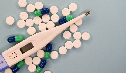 A top view of a heap of colourful pills and a thermometer and on blue background. Medical concept.