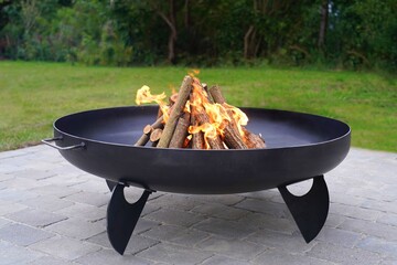 Iron fire pit and burning fire in a garden . - obrazy, fototapety, plakaty
