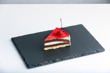 Piece of chocolate sponge cake with maraschino cherry. Side view to cake on black plate