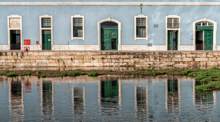 Fototapeta na wymiar building with blue and white walls and green doors reflected in a calm pond in the foreground