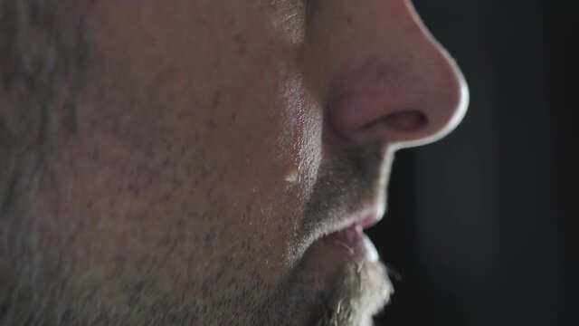 Close-up of a man's cheek with a tear sliding down it. A tear slowly descends on the distressed face of a men, macro.