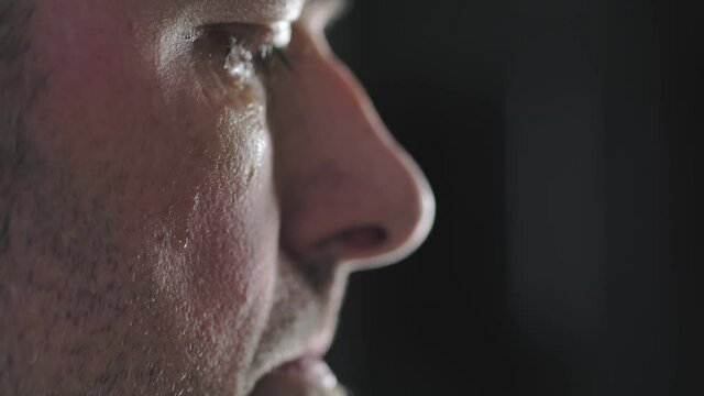 Close-up of a man's cheek with a tear sliding down it. A tear slowly descends on the distressed face of a men, macro.