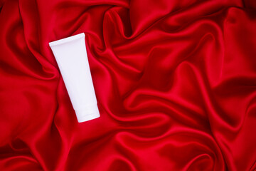 Tube of cream on a red satin background. Beauty care concept. Top view. Minimalism, mockup
