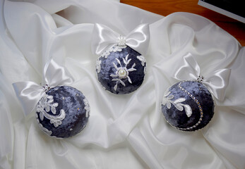 three handmade Christmas balls are decorated with white lace and rhinestones, the balls lie on a white cloth