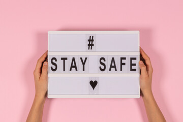 Hands holding lightbox with message Stay Safe on pink background. isolated. Healthcare, social distancing concept. Top view