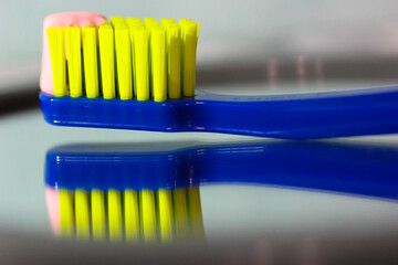 Blue toothbrush with green bristles close-up reflected in mirror, pink toothpaste. Oral hygiene and...