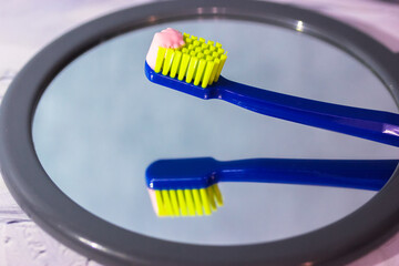 Blue toothbrush with green bristles close-up reflected in mirror, pink toothpaste. Oral hygiene and...
