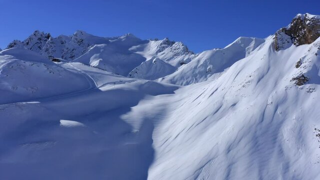 Mountain in winter - Drone flying above mountains covered with fresh snow in Tignes - Val d'Is&egrave;re, with a blue sky and a desert slope in background