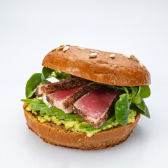 Bagel with tuna and greens on white background.
