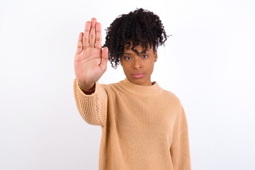 Young beautiful African American woman wearing knitted sweater against white wall doing stop...