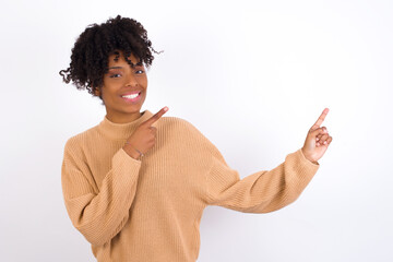 Young beautiful African American woman wearing knitted sweater against white wall, with positive...