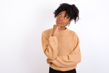 Fototapeta na wymiar Face expressions and emotions. Thoughtful Young beautiful African American woman wearing knitted sweater against white wall holding hand under his head, having doubtful look.
