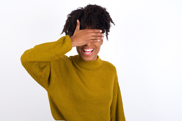 Fototapeta na wymiar Happy Young beautiful African American woman wearing knitted sweater closing eyes with hand going to see surprise prepared by friend standing and smiling in anticipation for something wonderful.