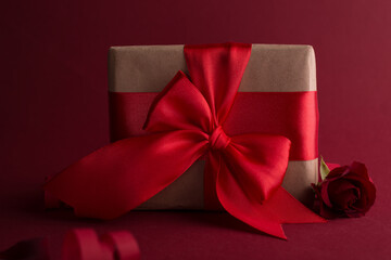 Close up Gift box with red silk bow against dark purple background. Valentines day romantic gift...