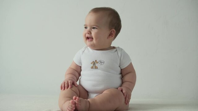 infant, childhood concept - happy funny playfull toddler kid 8 month baby girl learn to sit singly play on bed. smiling chubby active awake newborn crawl on knees indoors at home on white background