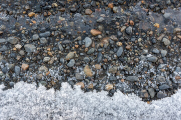 Icy lake shore with rocks pebbles and ice forming on the edge. Taken in fall autumn in northern Canada. Beautiful background graphic resource shot.