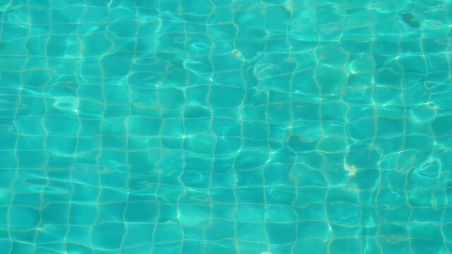 Wiggle picture of bottom of swimming pool, square green-blue tiles seen through clean water. Small random waves on surface create distortion and refraction of visible floor