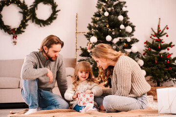 Parents give Christmas gifts box to their daughter while sitting in the room on the floor