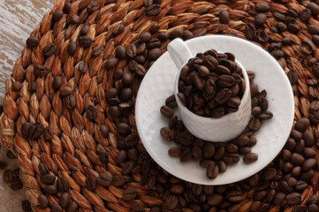 classic white espresso mug with coffee beans inside and a teapot in a black rustic background